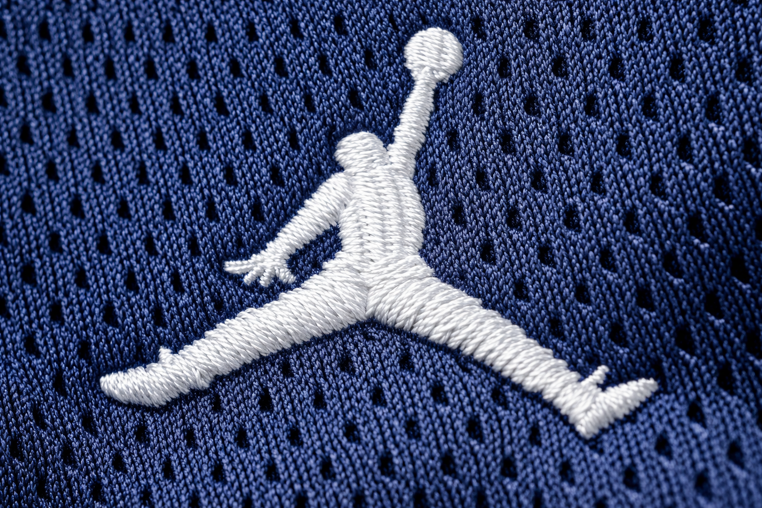 Michigan Wolverines: The Significance of the Jumpman 3 Macro close up of the stitched Jumpman logo and maize numbers on a Michigan jersey.