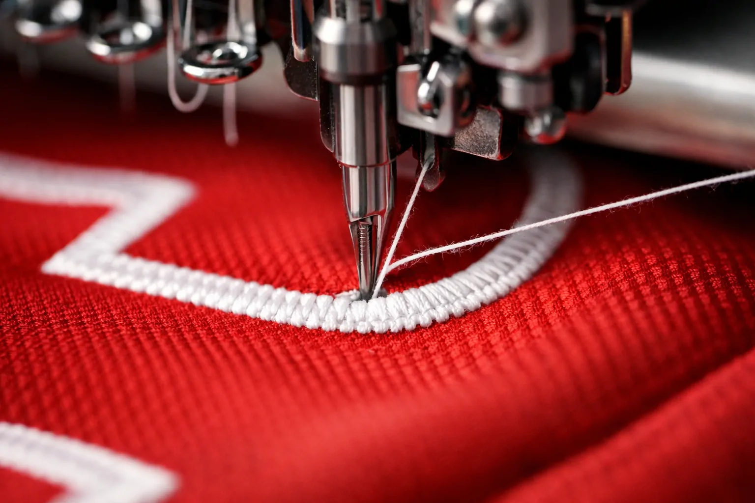 Close up of a sewing machine embroidering a team logo onto a red football jersey.
