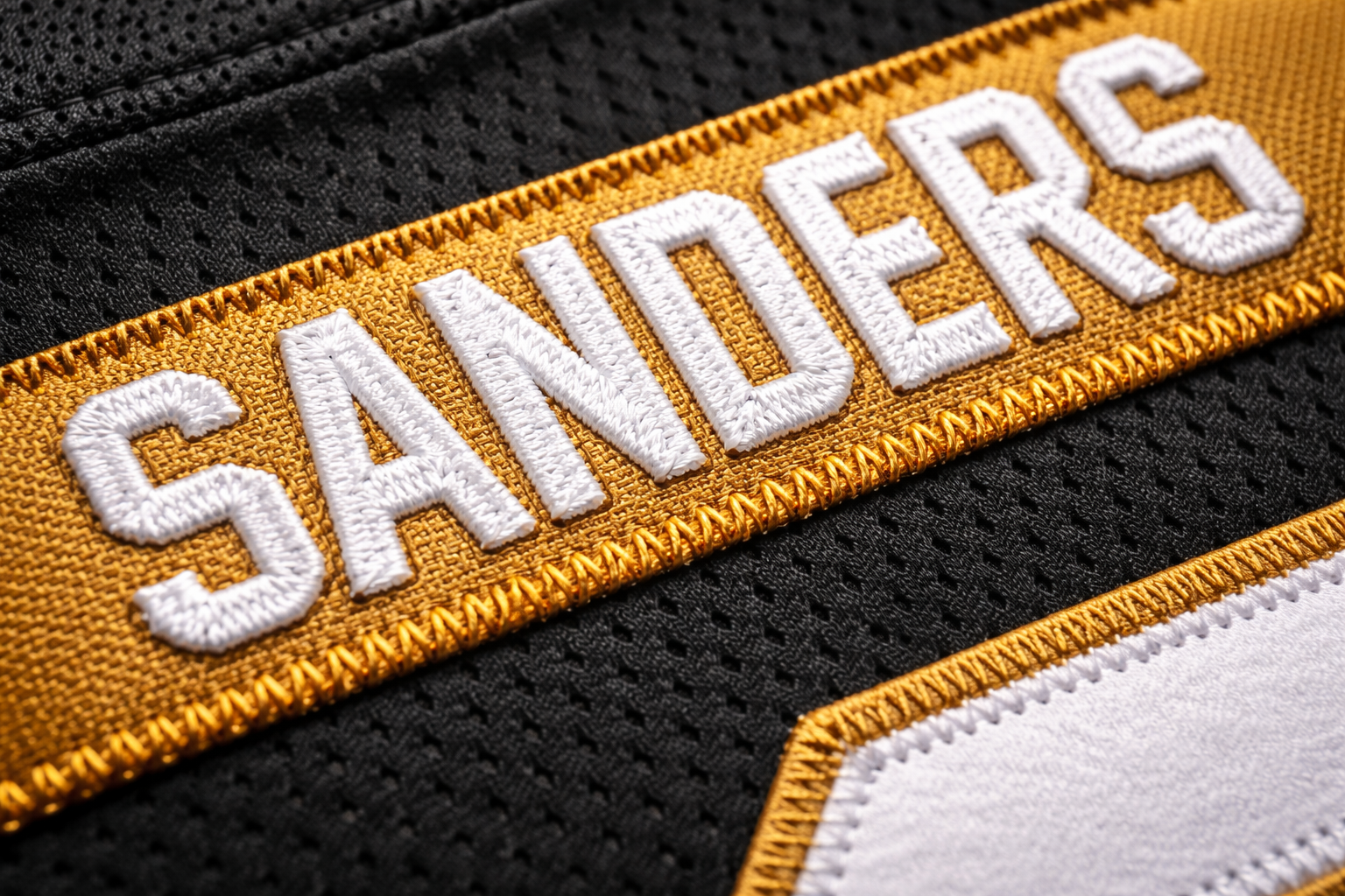Close up of the 'Sanders' nameplate stitched on a black football jersey.