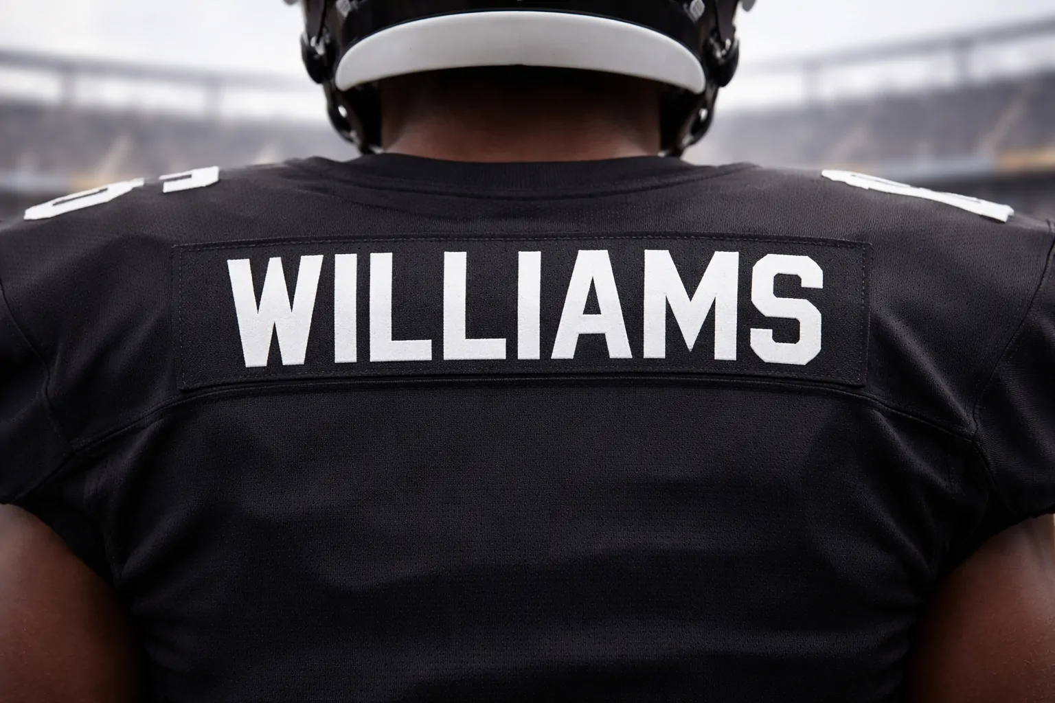 Back view of a fan wearing a black stitched football jersey with the nameplate clearly visible.