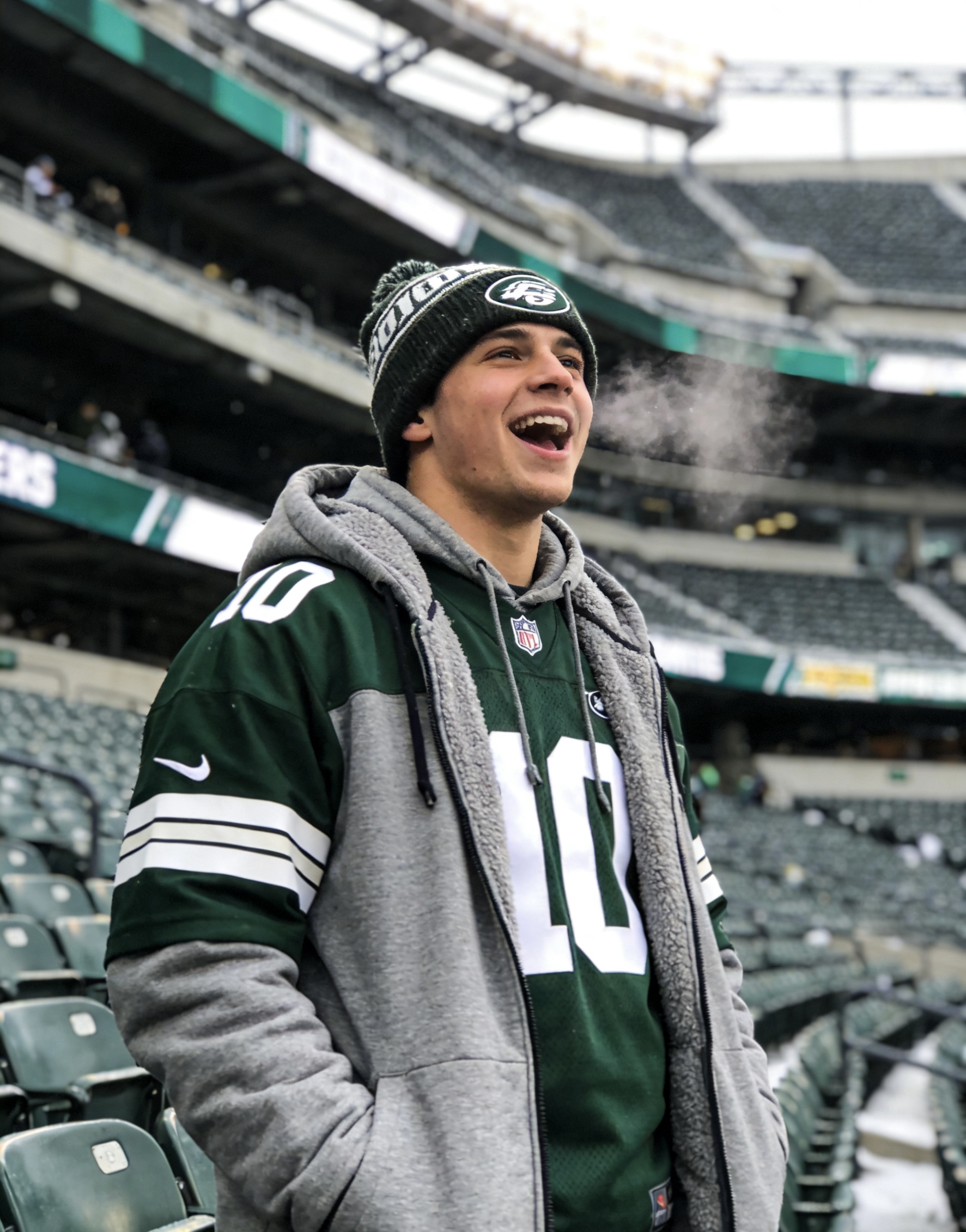 A fan wearing a football jersey over a heavy grey hoodie in a cold stadium.
