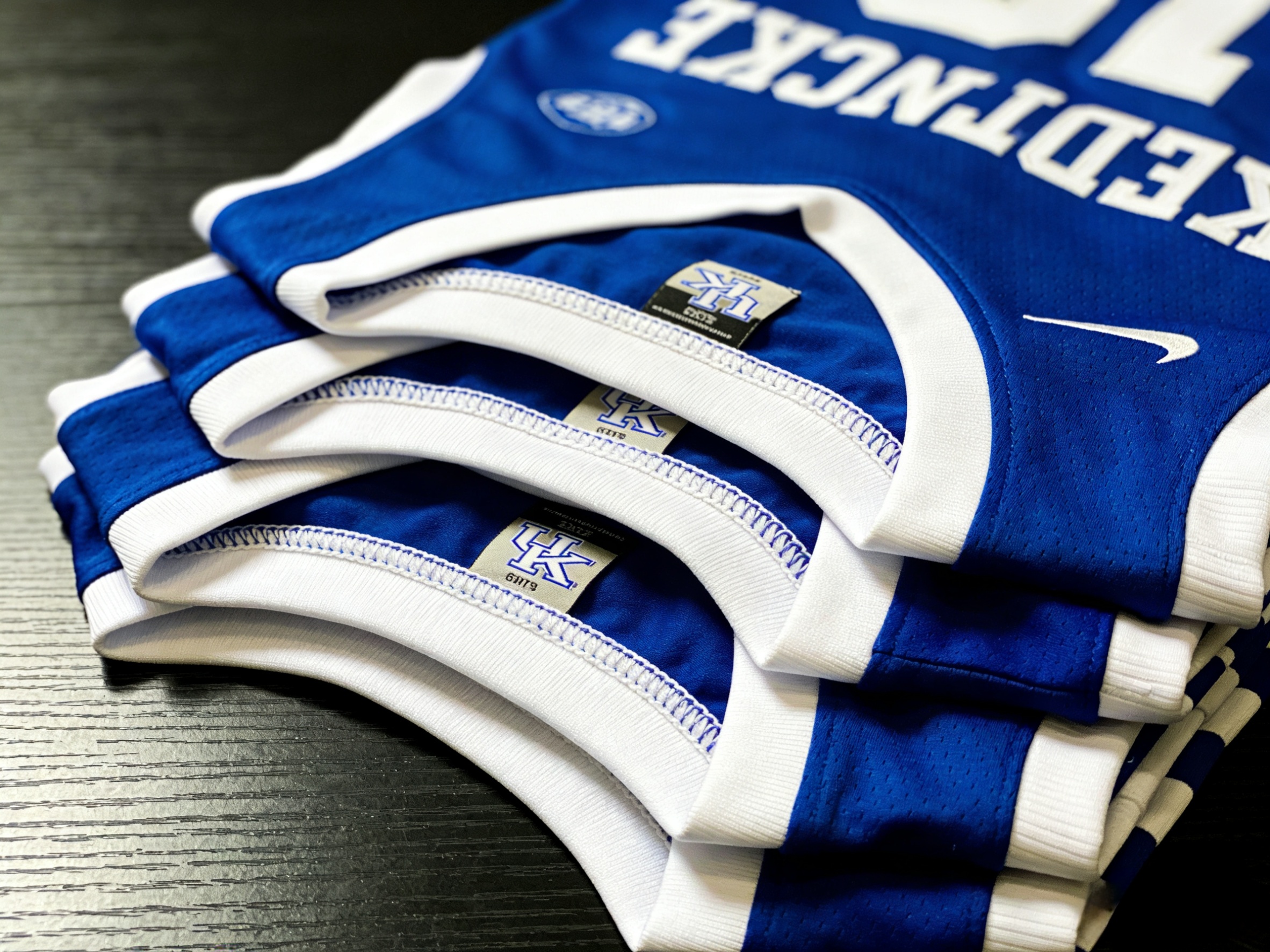 Neatly folded Kentucky Wildcats basketball jerseys in blue and white colors.