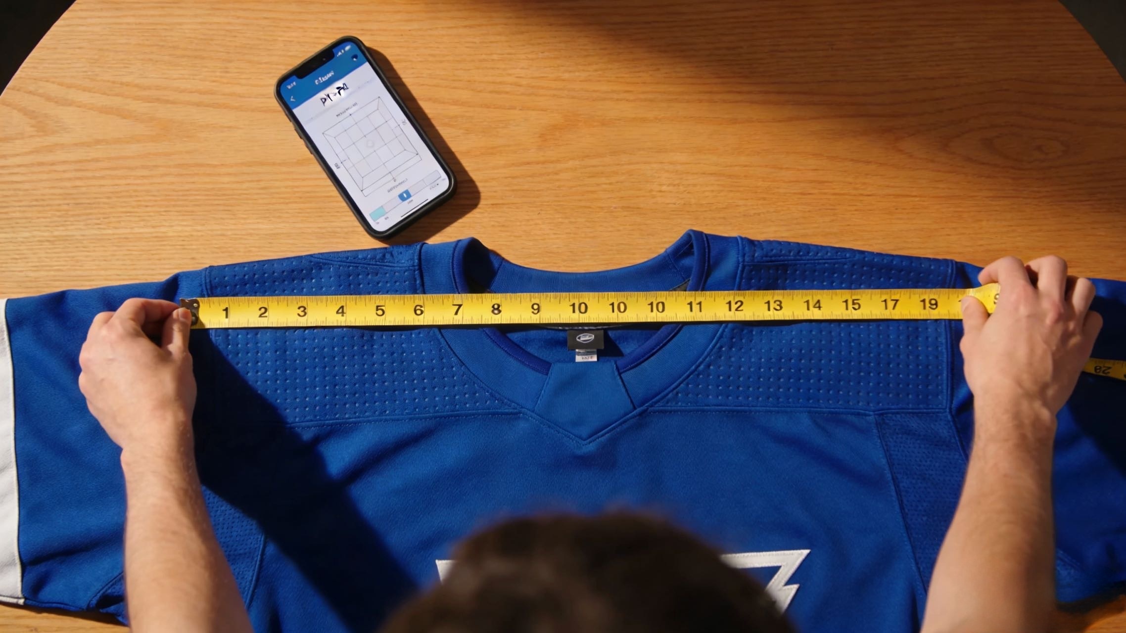A person measuring a hockey jersey to find the perfect fit using a size chart.