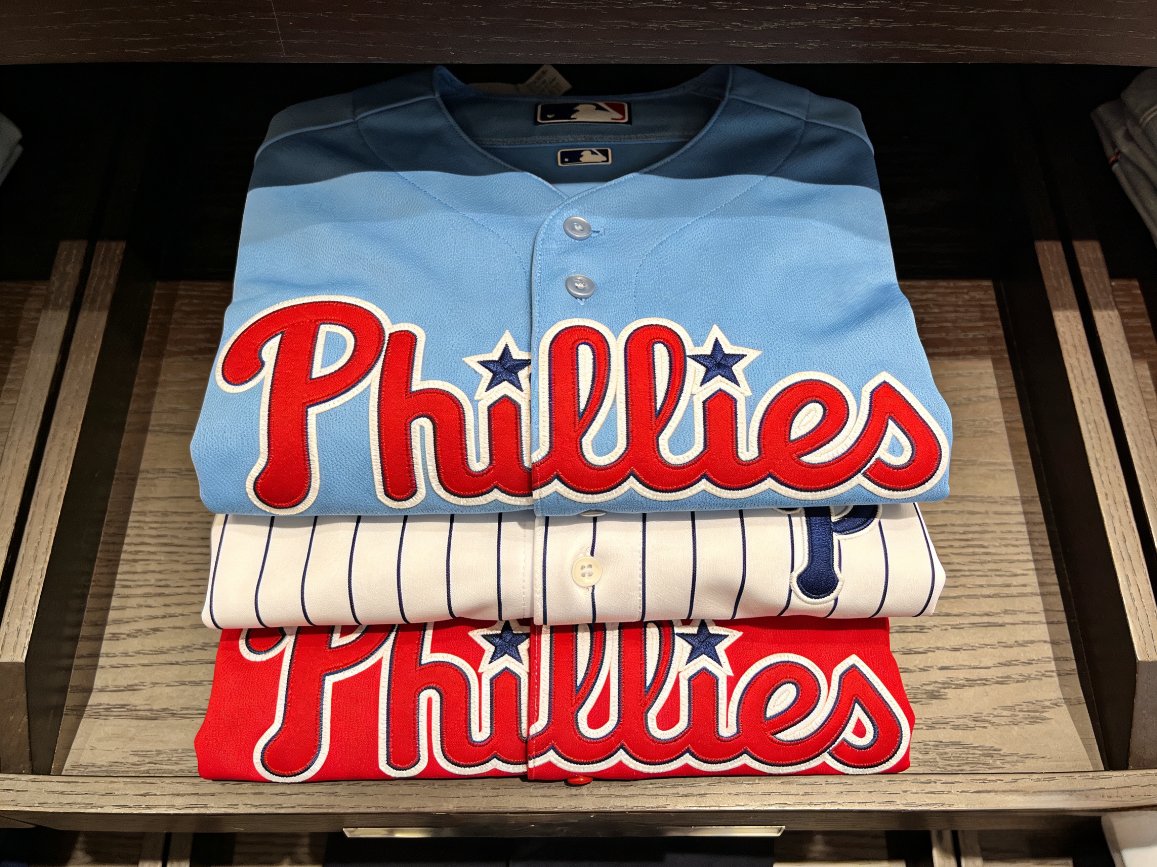 A stack of folded Philadelphia Phillies jerseys in various colors