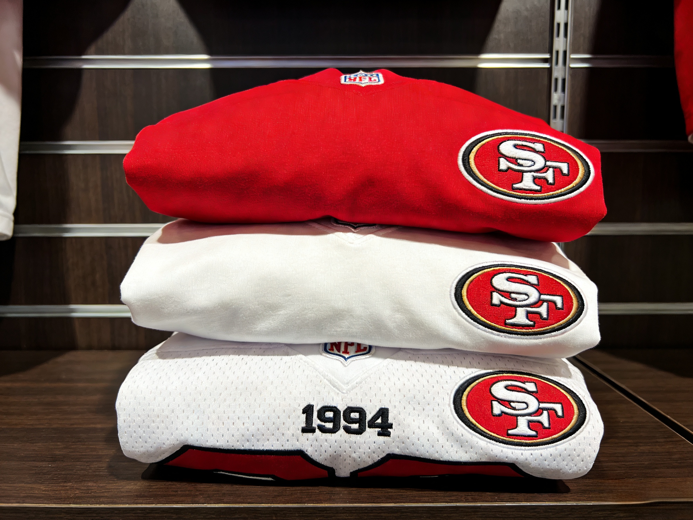  A stack of folded 49ers jerseys in red, white, and throwback styles